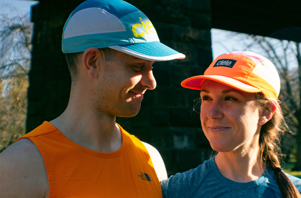 Eric and Claire Todd smile at each other, both wearing bright running gear, as they stand outside. 